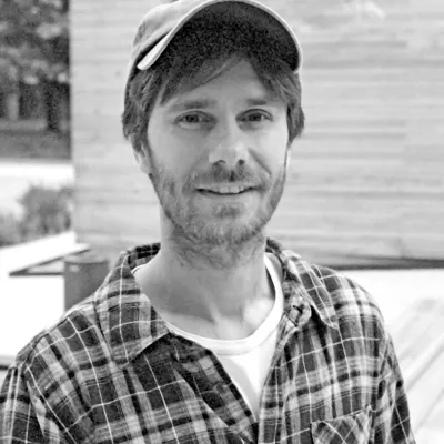 Porträt in schwarzweiß von Mathias Zinnen. Er trägt eine Kappe und ein kariertes Hemd